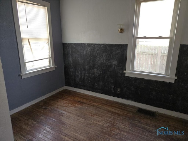 unfurnished room featuring dark wood-style floors, visible vents, and baseboards