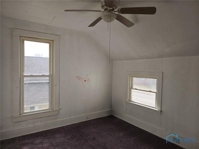 unfurnished room with vaulted ceiling, dark colored carpet, baseboards, and a healthy amount of sunlight