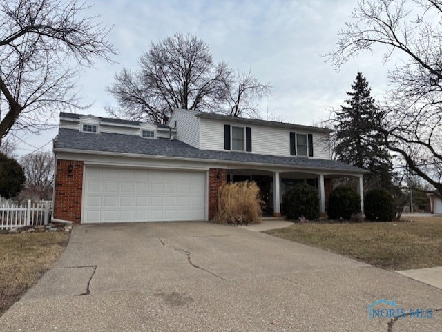 traditional-style house with fence, an attached garage, concrete driveway, a front lawn, and brick siding