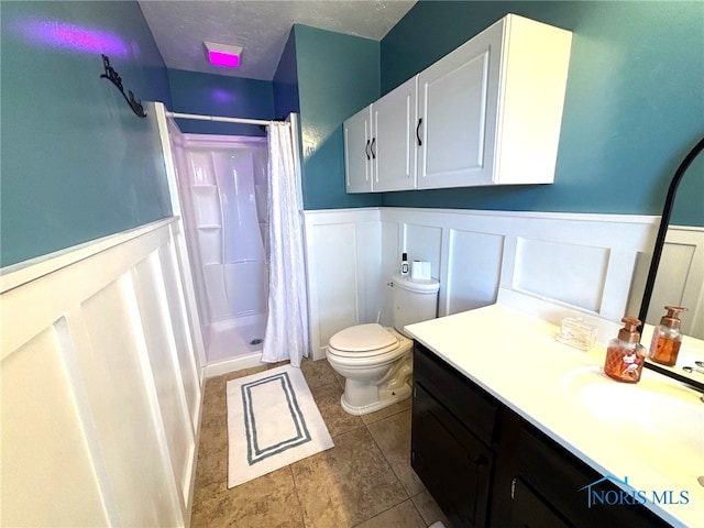 full bathroom with toilet, a textured ceiling, wainscoting, a shower stall, and vanity