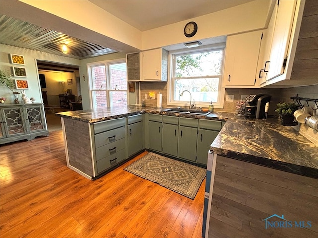 kitchen with a peninsula, light wood-style flooring, a sink, white cabinets, and tasteful backsplash