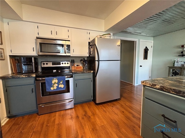 kitchen featuring white cabinetry, dark stone counters, wood finished floors, and appliances with stainless steel finishes