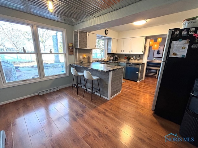 kitchen featuring dishwashing machine, visible vents, a peninsula, freestanding refrigerator, and dark countertops