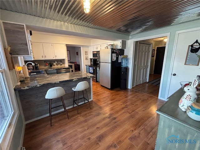 kitchen with dark countertops, a sink, appliances with stainless steel finishes, a peninsula, and dark wood-style flooring