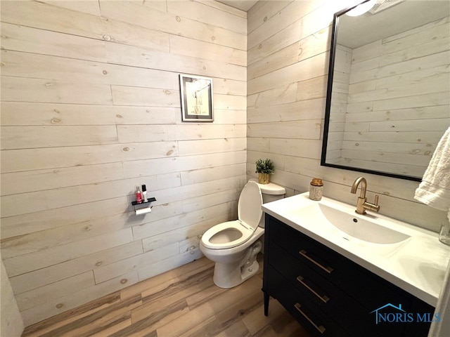 bathroom featuring wooden walls, toilet, vanity, and wood finished floors