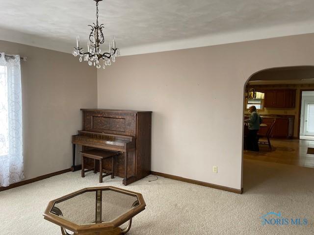 sitting room featuring arched walkways, an inviting chandelier, light carpet, and baseboards