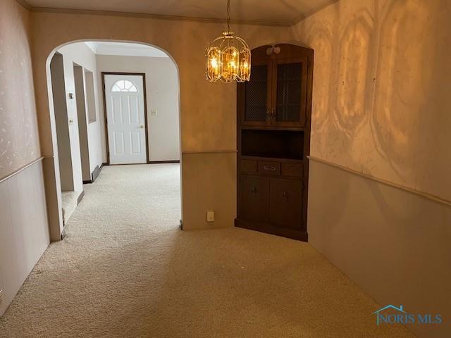 hall with arched walkways, light colored carpet, crown molding, and an inviting chandelier