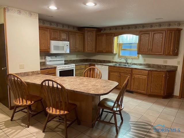 kitchen featuring brown cabinets, a peninsula, a kitchen breakfast bar, white appliances, and a sink