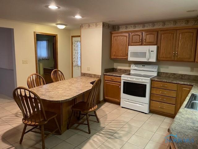 kitchen with brown cabinets, a peninsula, a kitchen breakfast bar, white appliances, and a sink