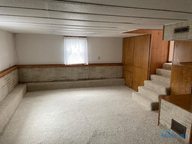 basement featuring stairway, carpet flooring, visible vents, and brick wall