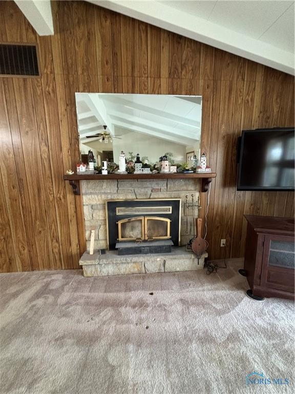 interior space featuring vaulted ceiling with beams, a stone fireplace, wood walls, carpet flooring, and visible vents