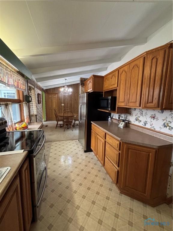 kitchen featuring beam ceiling, brown cabinets, a notable chandelier, dark countertops, and appliances with stainless steel finishes