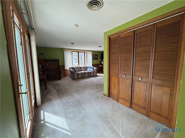 hall featuring light colored carpet, visible vents, wainscoting, wooden walls, and a textured ceiling