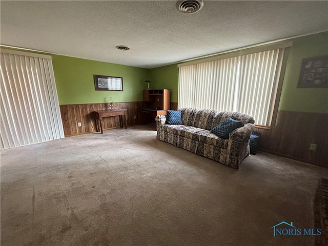 carpeted living room featuring a textured ceiling, wainscoting, visible vents, and wooden walls