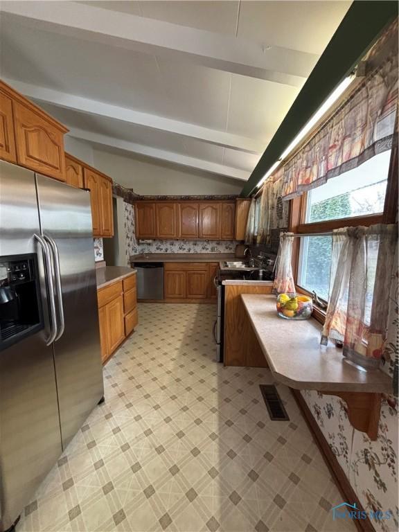 kitchen featuring lofted ceiling with beams, visible vents, appliances with stainless steel finishes, brown cabinets, and light floors