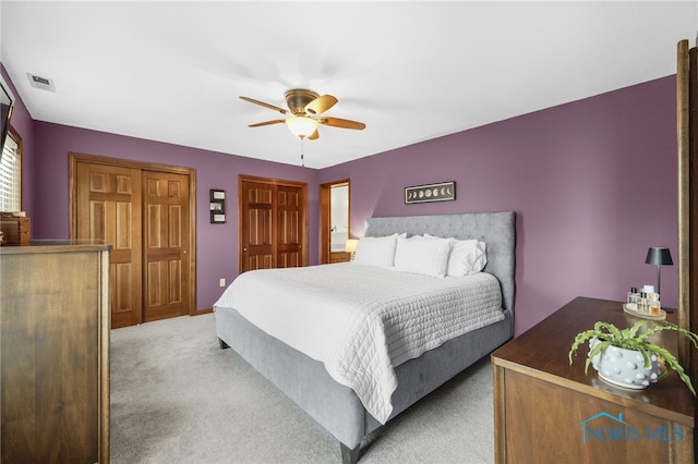 bedroom featuring ceiling fan, visible vents, multiple closets, and light colored carpet