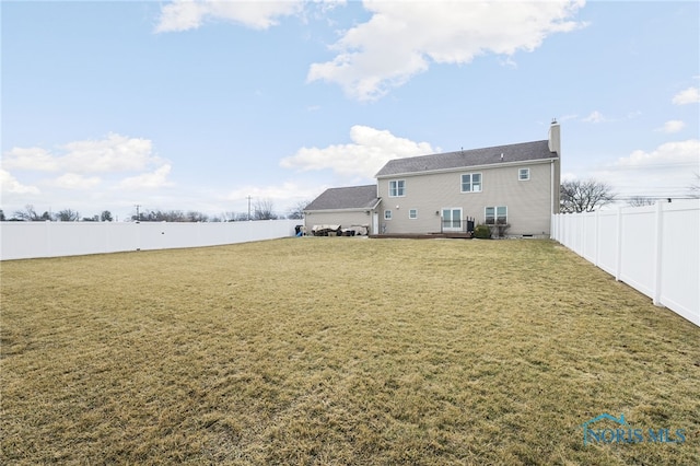 rear view of house featuring a fenced backyard, a chimney, and a lawn