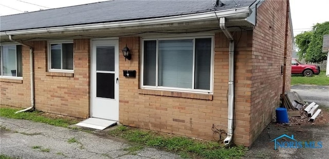 entrance to property with brick siding and roof with shingles