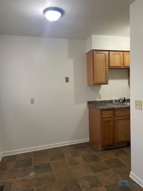 kitchen with dark countertops, brown cabinets, a sink, and baseboards