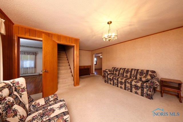 carpeted living room featuring wooden walls, stairway, crown molding, a baseboard heating unit, and a notable chandelier