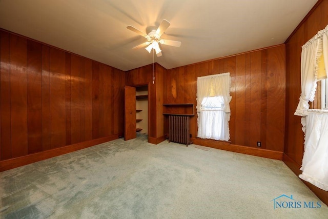 unfurnished bedroom featuring carpet, radiator, wood walls, and ceiling fan