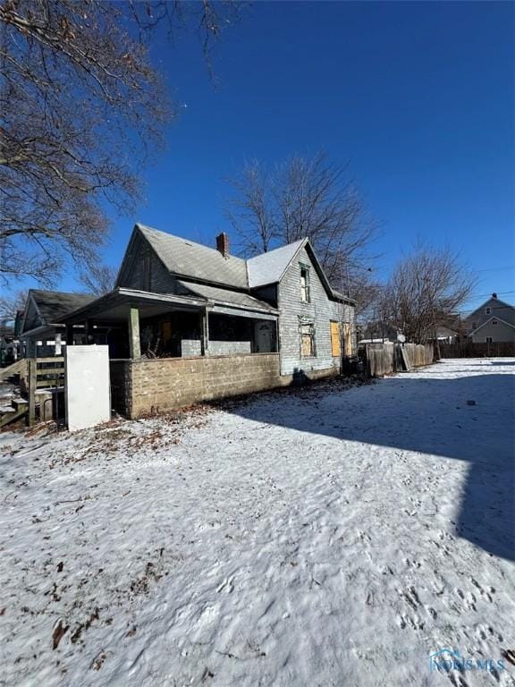 view of snow covered exterior with a chimney and fence