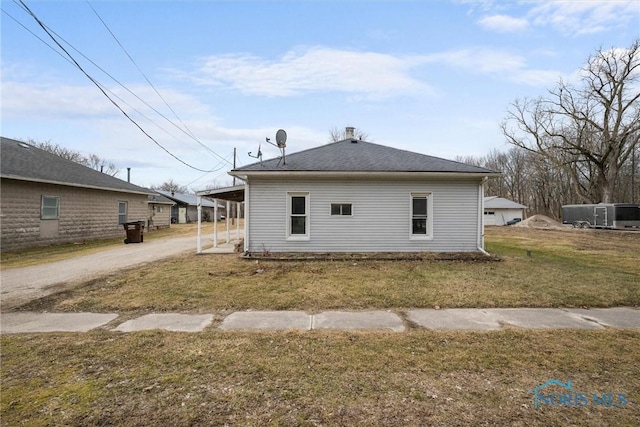 back of house featuring an attached carport, roof with shingles, a lawn, and driveway