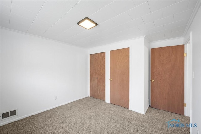 unfurnished bedroom featuring carpet floors, visible vents, baseboards, ornamental molding, and two closets