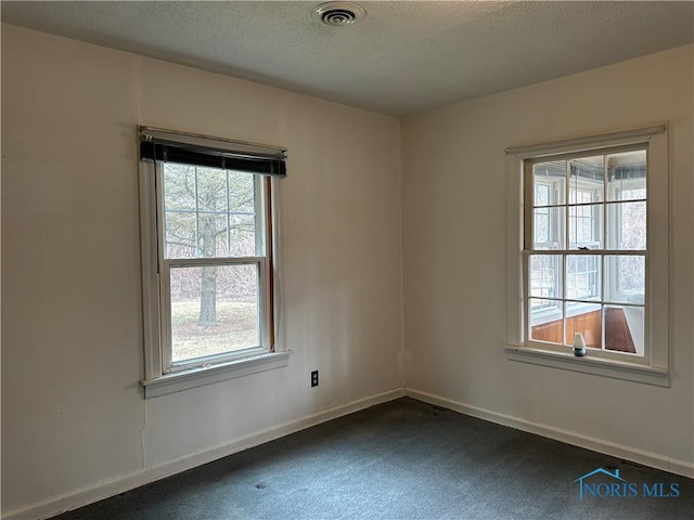 spare room with visible vents, a textured ceiling, baseboards, and dark colored carpet