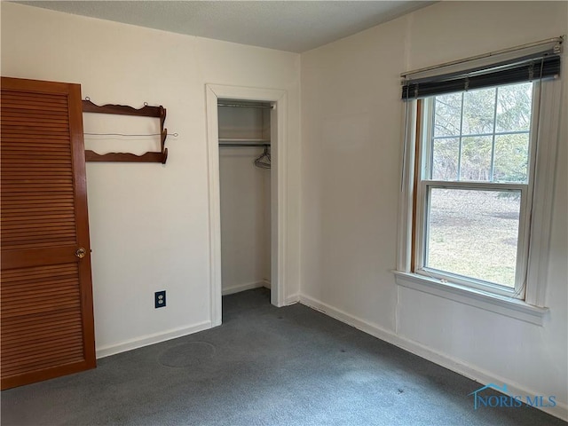 unfurnished bedroom with a closet, baseboards, and dark carpet