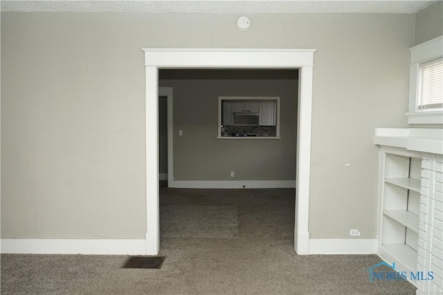 hallway with a textured ceiling, carpet, visible vents, and baseboards