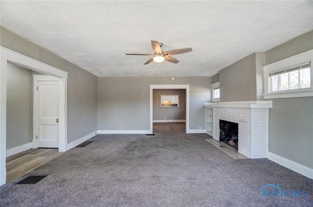 unfurnished living room featuring a brick fireplace, baseboards, visible vents, and a textured ceiling