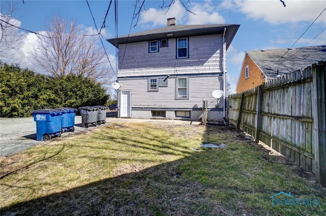rear view of property featuring fence, a lawn, and a chimney