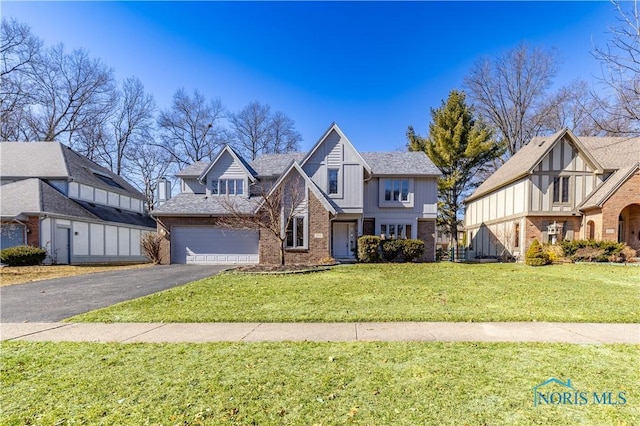 tudor house with brick siding, a front lawn, an attached garage, and driveway