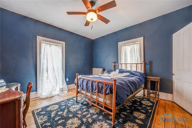 bedroom featuring baseboards, ceiling fan, radiator heating unit, and hardwood / wood-style flooring