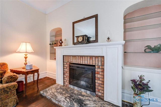 living area featuring a brick fireplace, baseboards, built in shelves, and hardwood / wood-style flooring