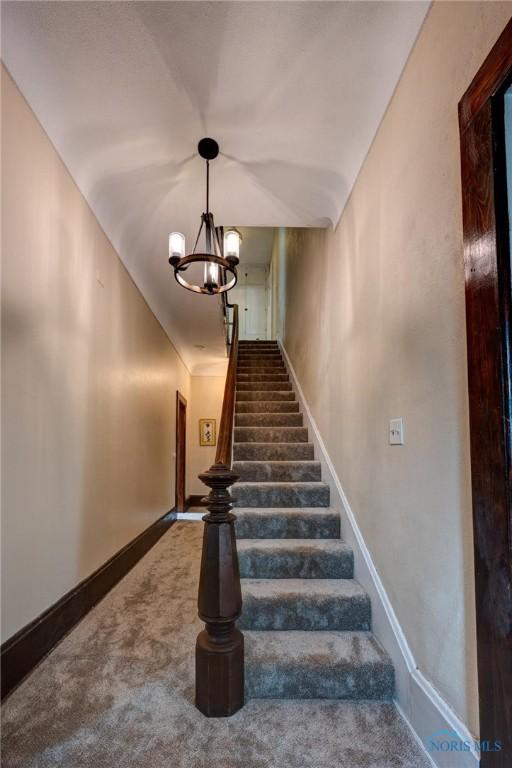 stairway with baseboards, an inviting chandelier, and carpet flooring