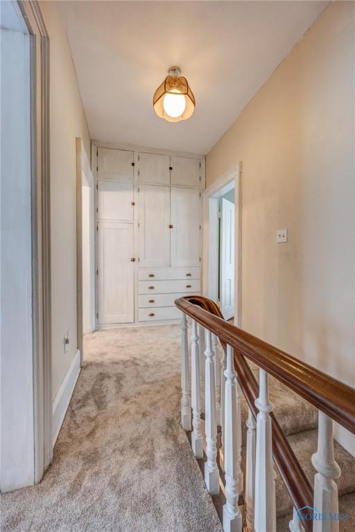 corridor with an upstairs landing and carpet