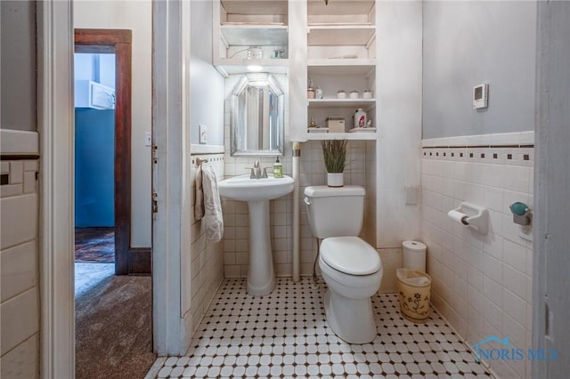 half bath featuring a sink, toilet, tile walls, and wainscoting