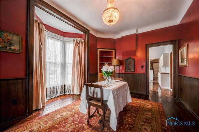 dining space featuring hardwood / wood-style floors, an inviting chandelier, wood walls, and wainscoting