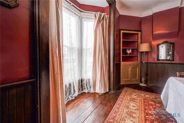 bedroom featuring a wainscoted wall, wood walls, and dark wood-style flooring