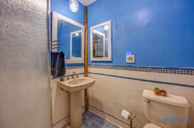 bathroom with a wainscoted wall, toilet, and tile walls