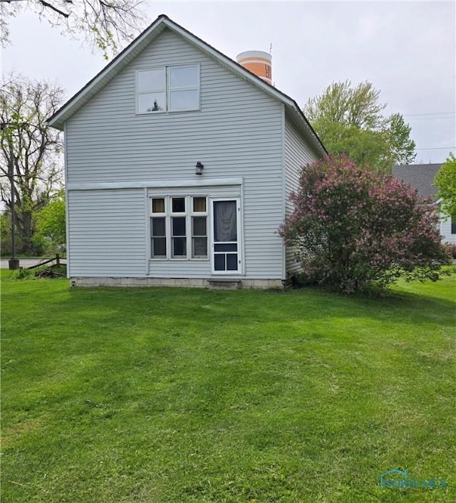 rear view of property featuring a lawn and a chimney