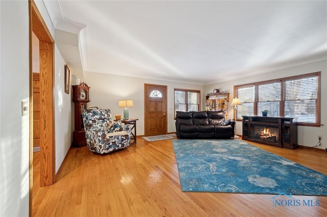 living area with light wood-style floors, a warm lit fireplace, and baseboards