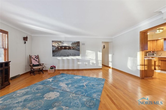 living area with light wood-style floors, baseboards, visible vents, and crown molding