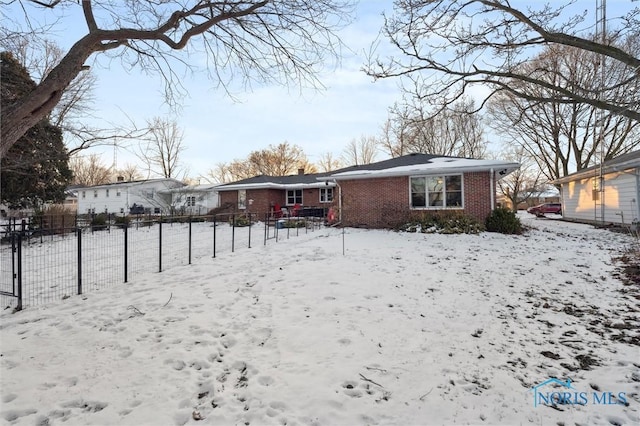 snow covered back of property featuring brick siding, fence, and a chimney