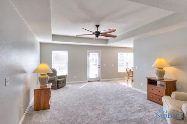 living area with a wealth of natural light, a raised ceiling, carpet flooring, and baseboards