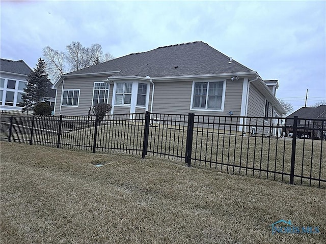 back of property with roof with shingles, a yard, and fence