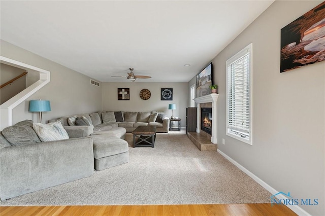 living area featuring visible vents, a glass covered fireplace, ceiling fan, wood finished floors, and baseboards