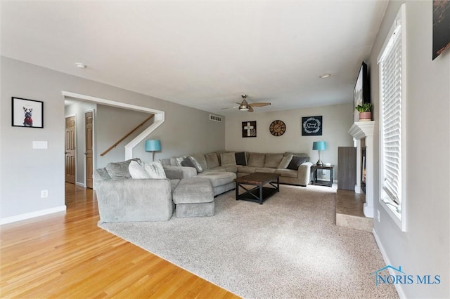 living room featuring ceiling fan, a fireplace, wood finished floors, visible vents, and baseboards